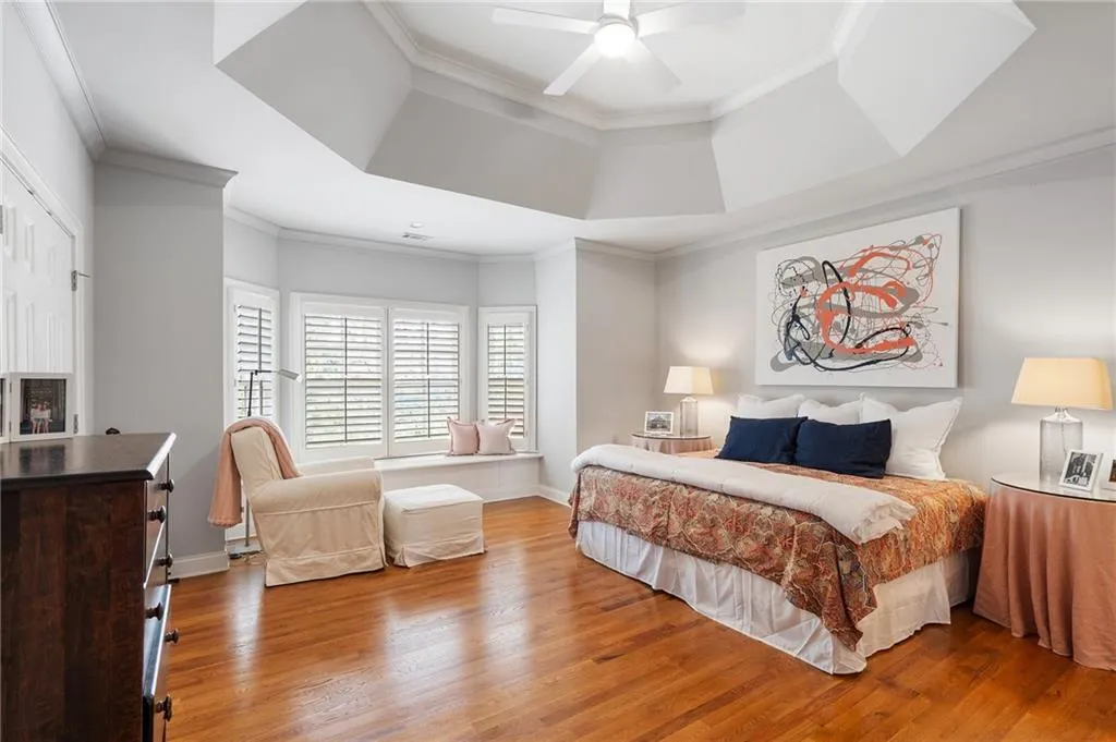 Bedroom featuring crown molding, light hardwood / wood-style flooring, a raised ceiling, ceiling fan, and a fireplace