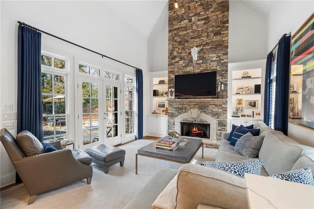 Living room with high vaulted ceiling, a stone fireplace, and built in features