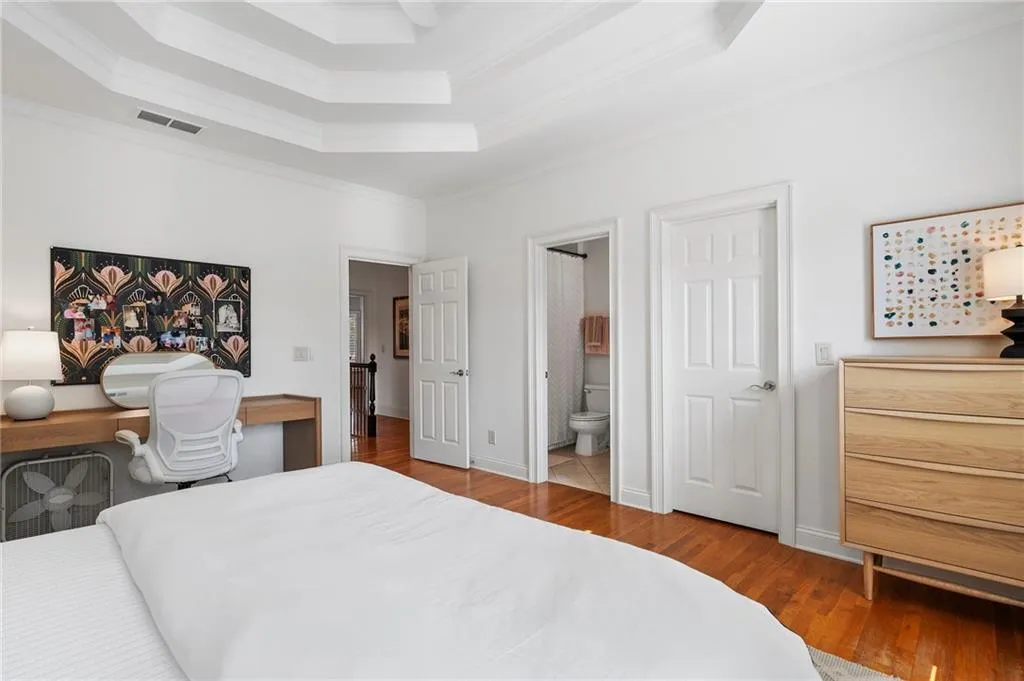 Bedroom with hardwood / wood-style floors, a tray ceiling, ensuite bath, and ornamental molding