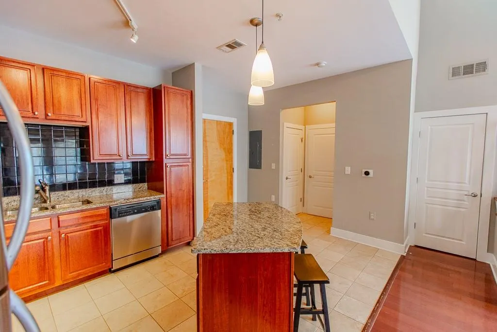 Kitchen with stainless steel dishwasher, decorative light fixtures, light stone counters, track lighting, and backsplash Kitchen with stainless steel dishwasher, decorative light fixtures, light stone counters, track lighting, and backsplash