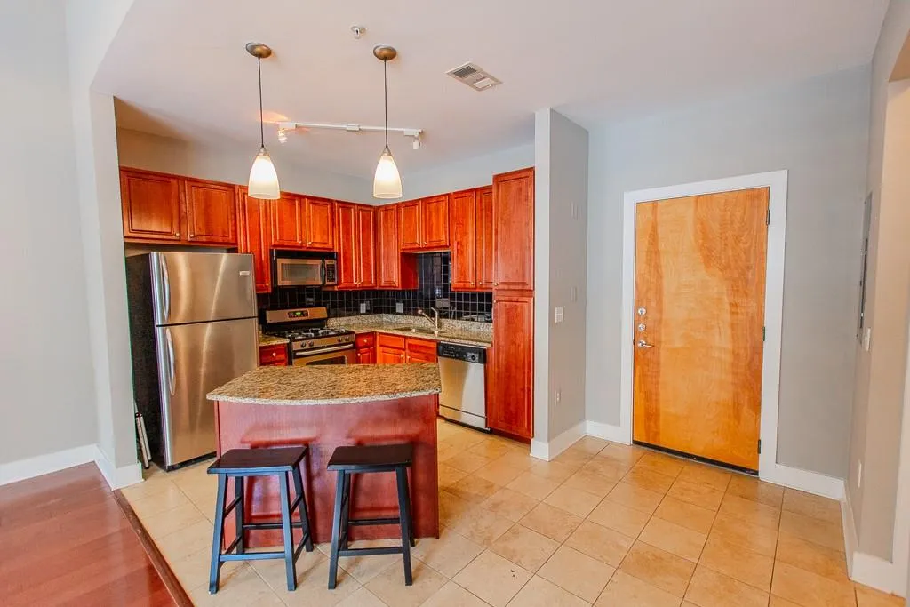 Kitchen featuring a kitchen island, stainless steel appliances, hanging light fixtures, tasteful backsplash, and a kitchen bar Kitchen featuring a kitchen island, stainless steel appliances, hanging light fixtures, tasteful backsplash, and a kitchen bar