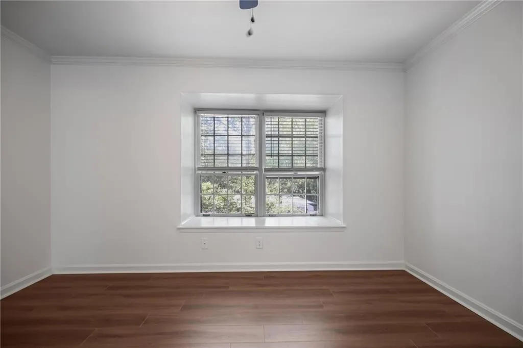 Wood-finish flooring, white walls, double-pane window with blinds, crown molding, and a window seat