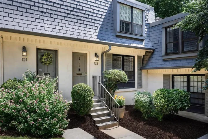 Slate gray shingle roofing, dormer windows, exterior wall sconces, dark gray entry doors, and mature landscaping