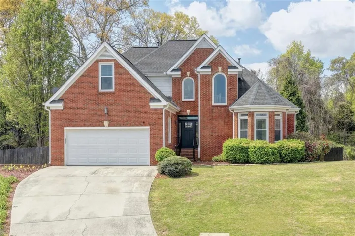 Traditional brick exterior with white trim, arched windows, an integrated two-car garage, and a bay window feature