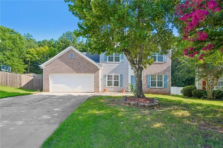 Brick and siding exterior, two-car garage, mature trees, manicured lawn, and a paved driveway