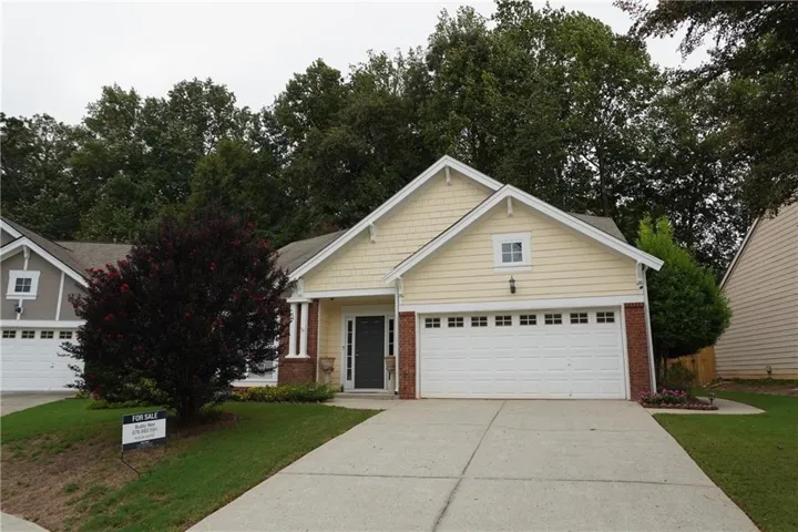 Single-story residence featuring light yellow siding, brick accents, a two-car garage, and a concrete driveway