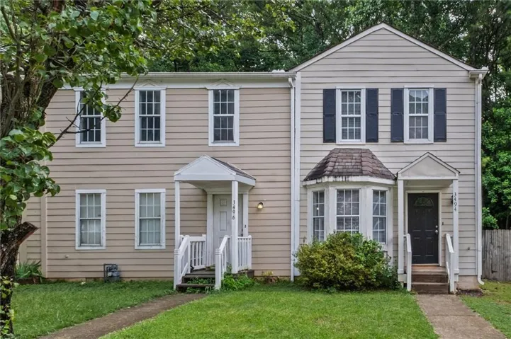 Two-story duplex featuring horizontal siding, white-framed windows, and a manicured lawn
