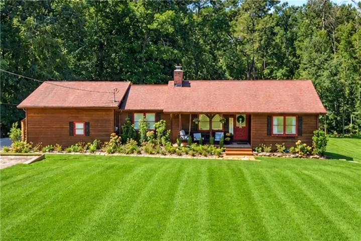 Single-story wood-sided exterior with a red shingle roof, complemented by a covered front porch and a prominent red entry door