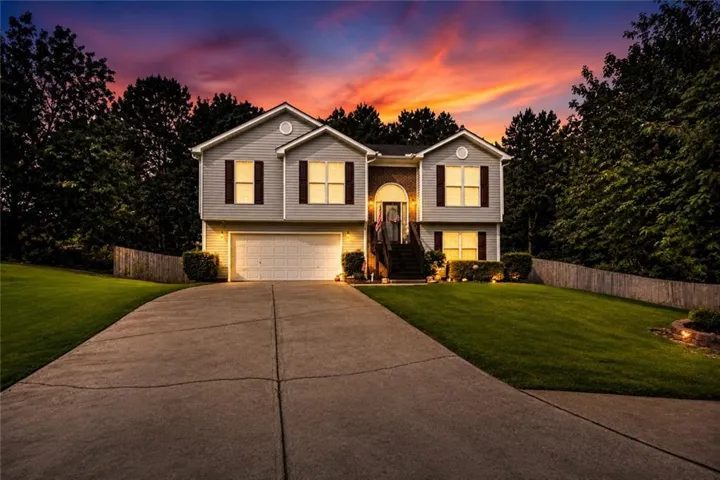 Split-level home featuring light gray siding, dark window shutters, and a two-car garage