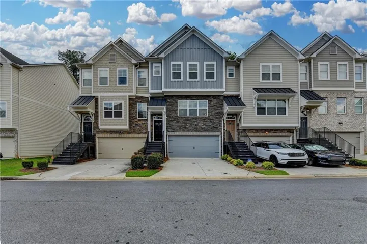Contemporary multi-level townhome featuring a mixed-material facade with stone veneer and horizontal siding, an attached garage, and a covered entry with a black metal handrail