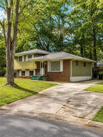Split-level residence featuring brick and siding exterior, front porch with white railing, concrete driveway, and mature trees