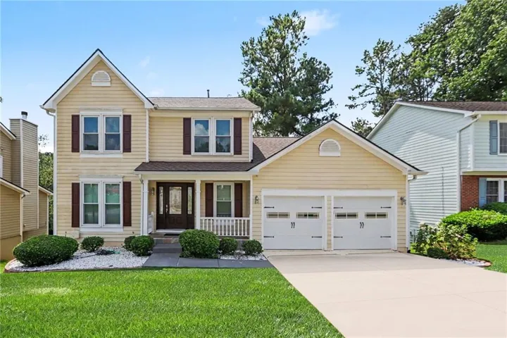 Two-story exterior with light-colored siding, a covered front porch, and a two-car garage