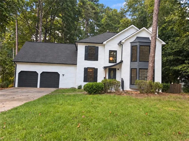 Two-story property featuring white siding and brick, a two-car garage with dark paneled doors, and a prominent bay window with dark trim
