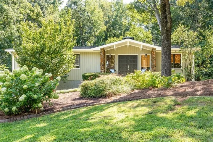 Siding exterior with stone veneer accents, a prominent gable roof, and lush landscaping