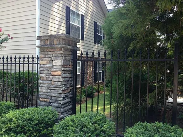 Left side view of the buildingblack wrought iron fence, manicured shrubs, and mature trees