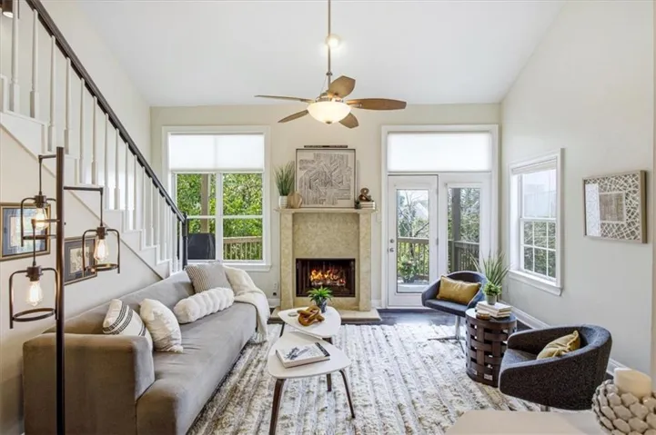 Living area featuring a stone fireplace, double French doors, large windows, and a ceiling fan