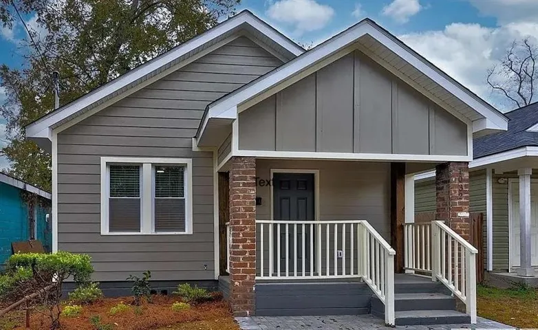 Gray siding exterior with white trim, a covered front porch, brick and wood porch columns, and a dark front door