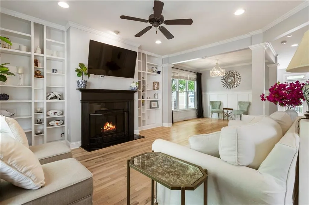 Living room with ornate columns, ornamental molding, a ceiling fan, wood finished floors, and a fireplace with flush hearth