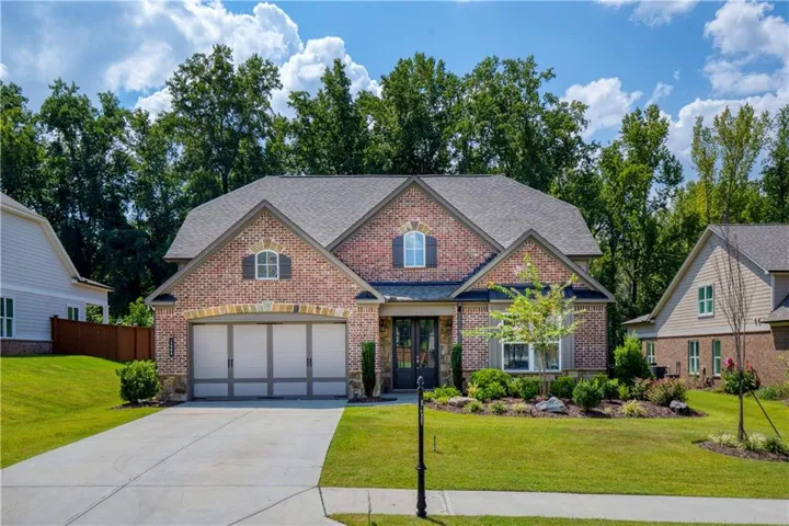 Brick and stone facade, arched entryway, two-car garage, mature landscaping, and concrete driveway
