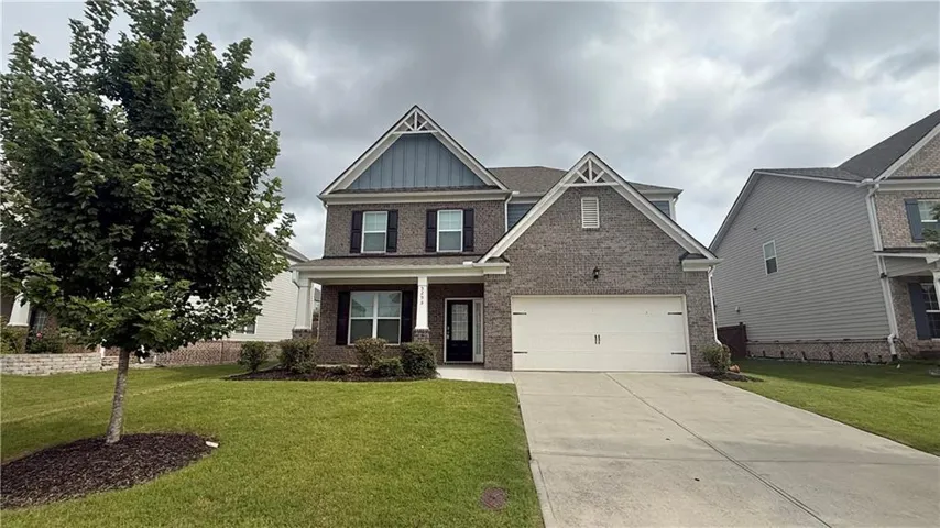 Two-story brick and siding residence featuring a two-car garage, established front landscaping, covered porch, and a concrete driveway