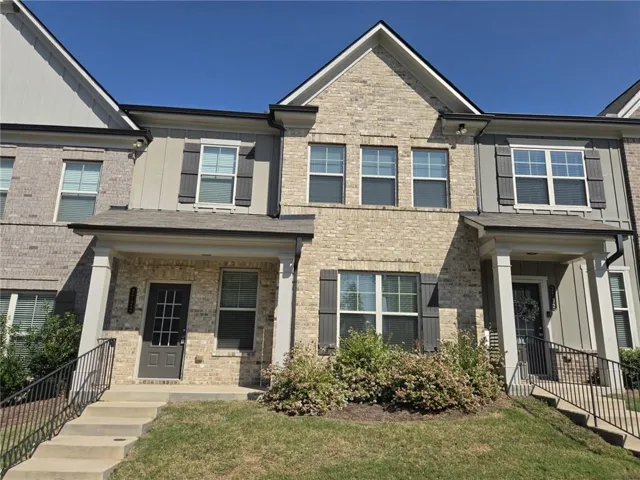 Two-story residence featuring a brick facade with complementary siding accents, multiple gabled rooflines, a covered front porch with substantial columns, and integrated exterior lighting