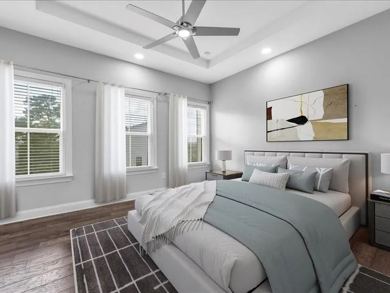 Bedroom with a tray ceiling, wood finished floors, multiple windows, recessed lighting, and ceiling fan