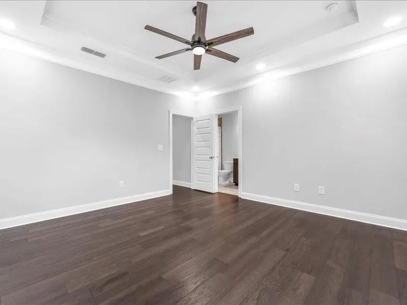 Empty room featuring a tray ceiling, a ceiling fan, ornamental molding, dark wood-style floors, and recessed lighting