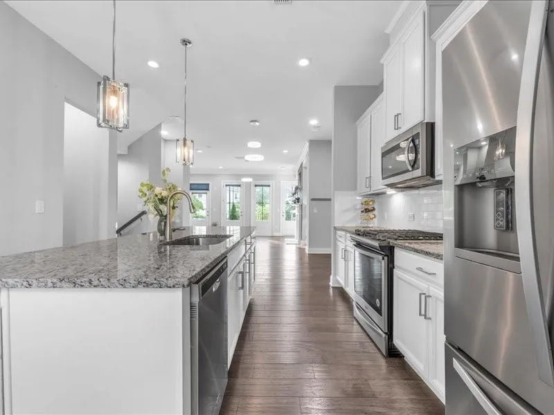 Kitchen featuring stainless steel appliances, a center island with sink, dark wood-type flooring, white cabinets, and tasteful backsplash