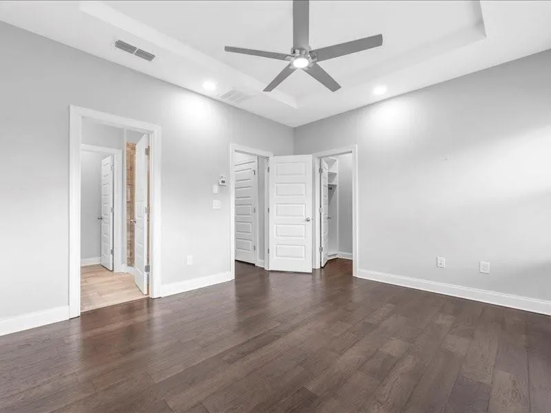 Unfurnished bedroom with recessed lighting, dark wood finished floors, a raised ceiling, and a walk in closet
