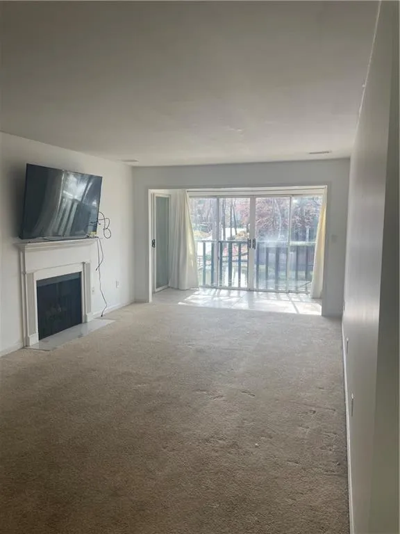 Unfurnished living room featuring a fireplace with flush hearth, visible vents, and light colored carpet