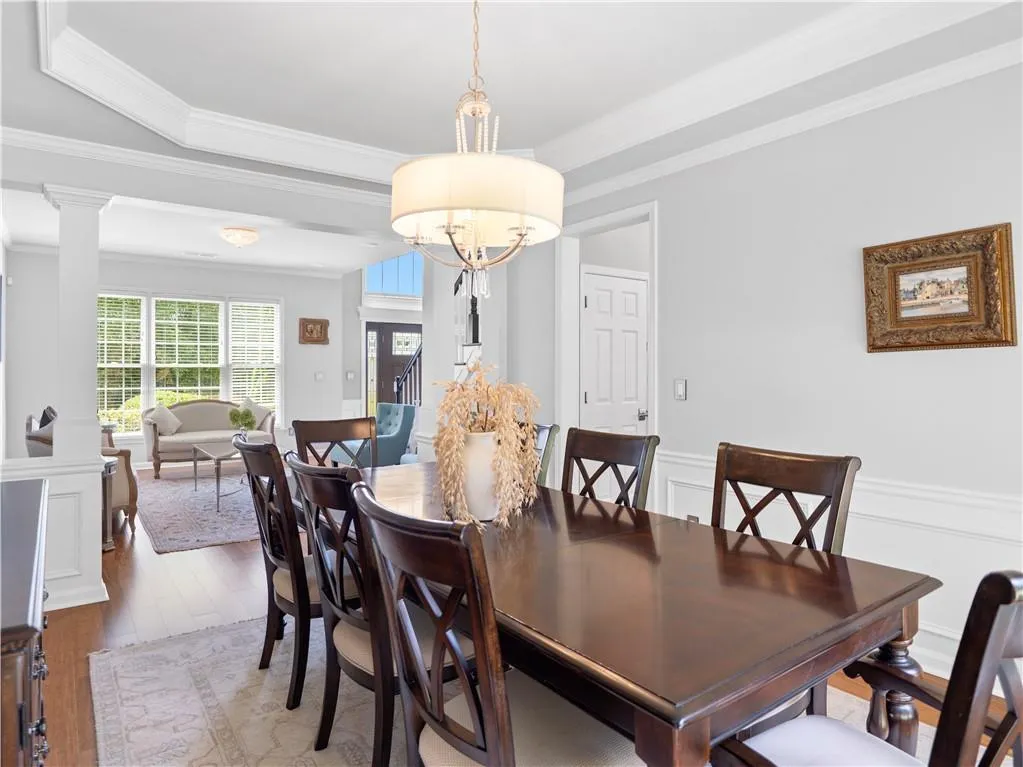 Dining space with a notable chandelier, wood-type flooring, ornamental molding, a tray ceiling, and ornate columns