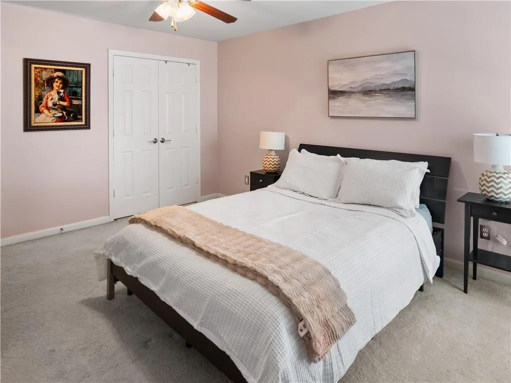 Bedroom with ceiling fan, light colored carpet, and a closet