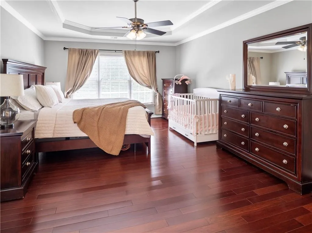 Bedroom featuring ceiling fan, dark wood-type flooring, a tray ceiling, and crown molding