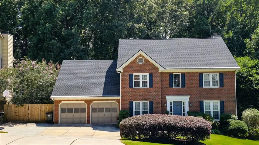 Brick exterior with a prominent two-story facade, featuring a two-car garage, white window frames with dark shutters, and a front entry with a blue door
