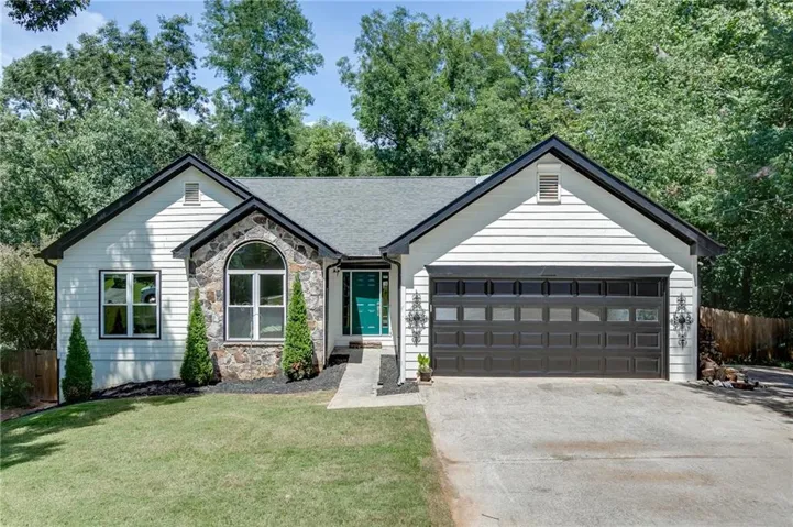 White horizontal siding exterior with stone accents, an arched window, and a dark garage door