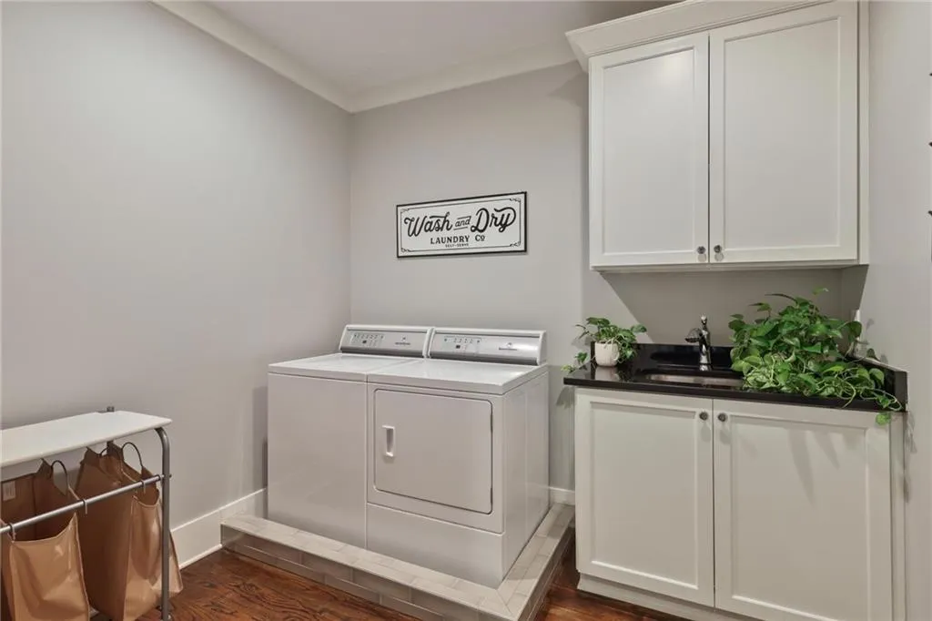 Laundry room with dark hardwood / wood-style flooring, washing machine and dryer, crown molding, sink, and cabinets