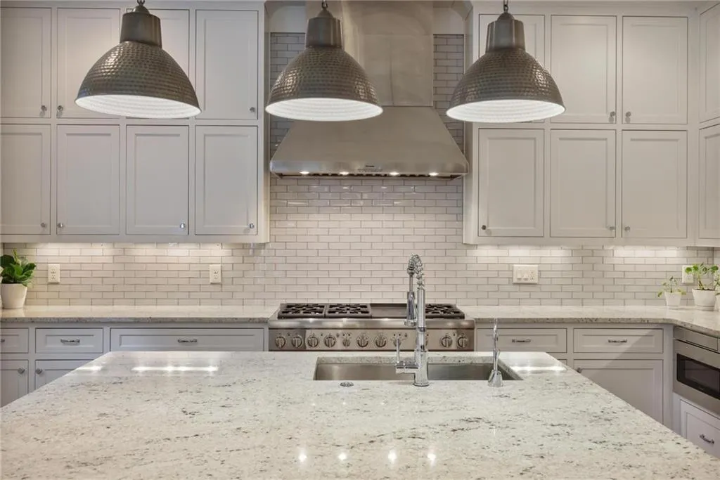 Kitchen with wall chimney range hood, light stone counters, tasteful backsplash, and stainless steel microwave