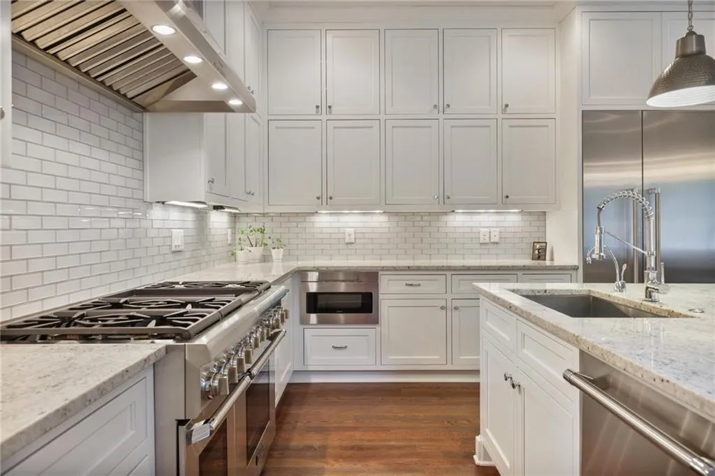 Kitchen with backsplash, decorative light fixtures, custom exhaust hood, dark wood-type flooring, and premium appliances