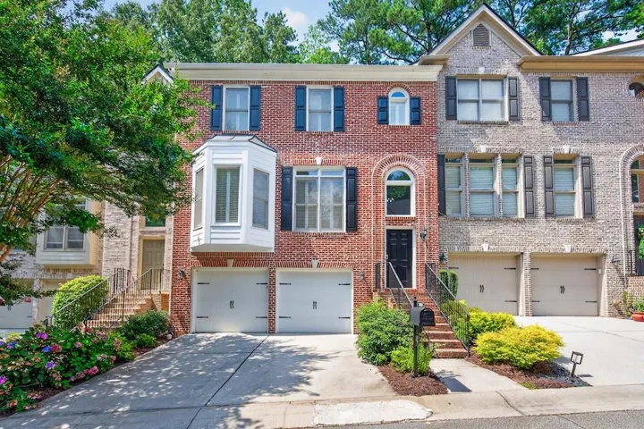 Brick townhome featuring a prominent bay window with white siding, a two-car garage, and a black paneled front door with an arched transom
