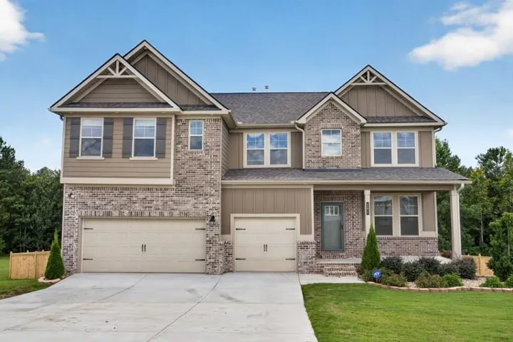 Two-story residence featuring a brick and siding exterior, dual garage doors, a covered front porch, and a well-maintained lawn