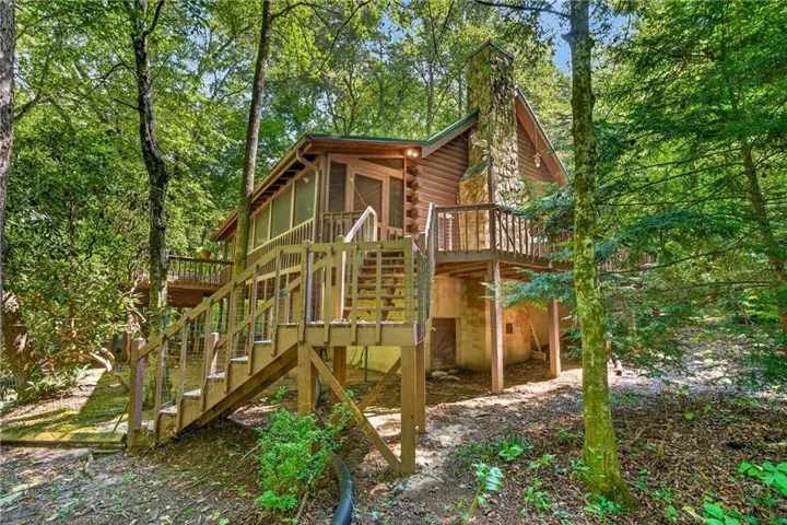 Wood-sided exterior featuring a prominent stone chimney, multiple outdoor decks, and a screened porch