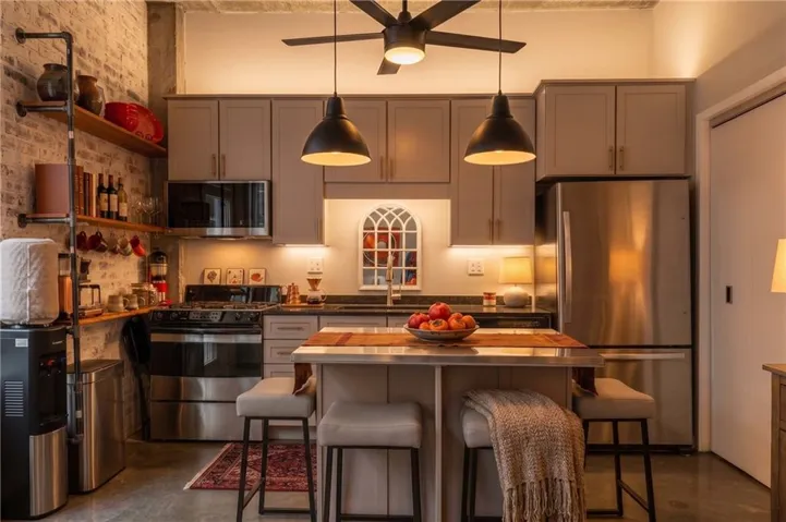 Kitchen featuring exposed brick, stainless steel appliances, custom shelving, a ceiling fan, and pendant lighting