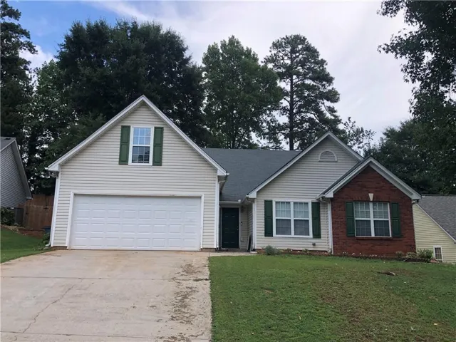 Exterior with light-colored siding and brick accents, featuring a two-car garage, dark green shutters, and a sloped lawn