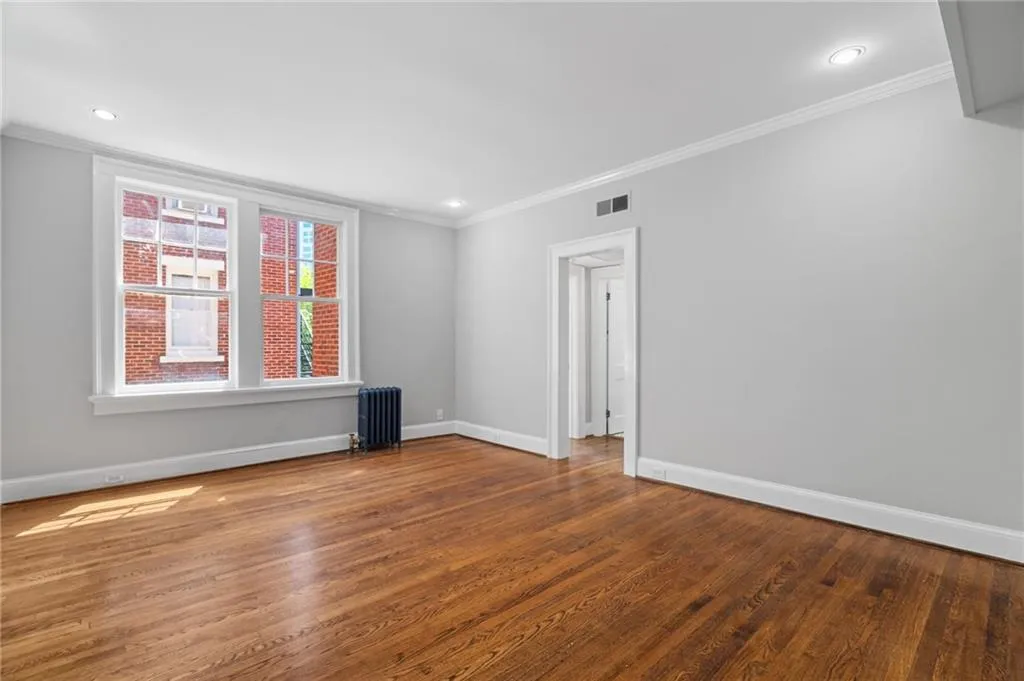 Spare room with radiator, ornamental molding, visible vents, wood finished floors, and baseboards Spare room with radiator, ornamental molding, visible vents, wood finished floors, and baseboards