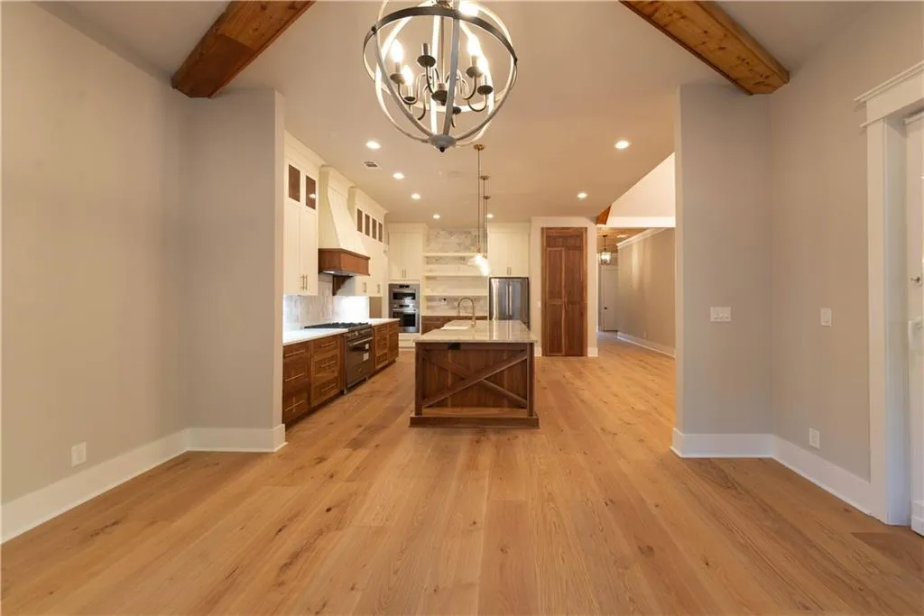 Kitchen with appliances with stainless steel finishes, a kitchen island with sink, pendant lighting, beam ceiling, and an inviting chandelier