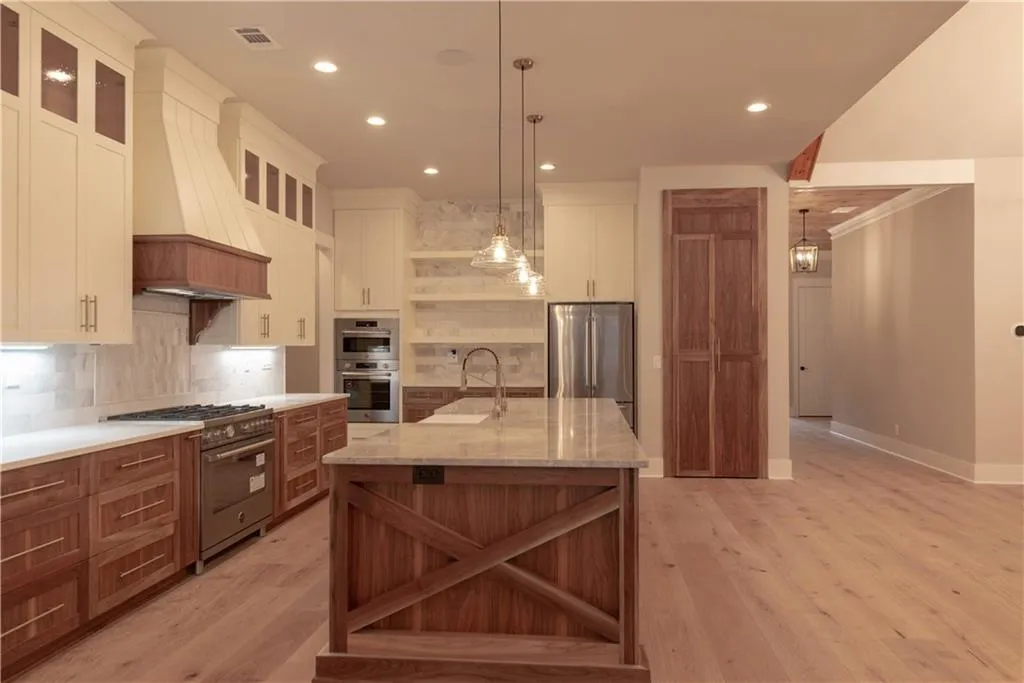 Kitchen with appliances with stainless steel finishes, backsplash, custom exhaust hood, decorative light fixtures, and a large island