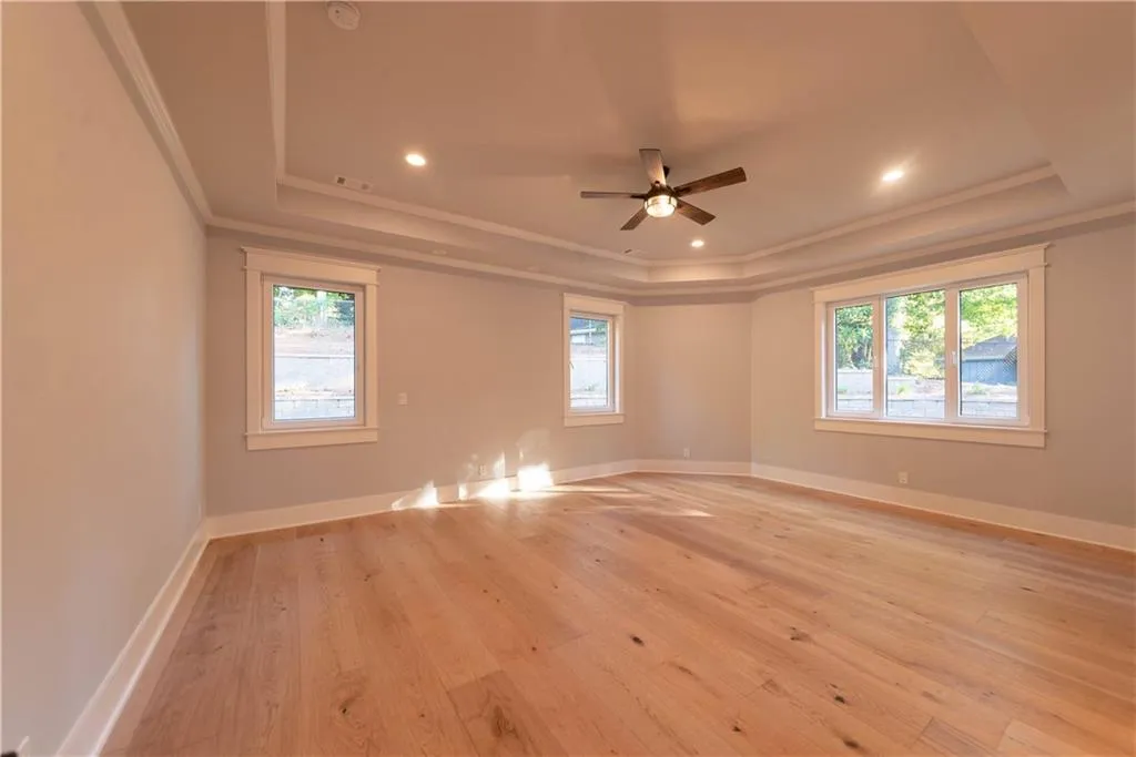 Empty room with a tray ceiling, light hardwood / wood-style flooring, ceiling fan, and a healthy amount of sunlight