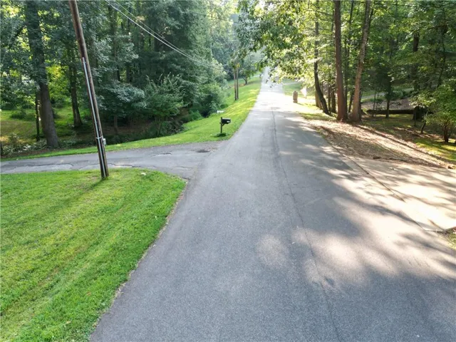 Paved road with a gravel shoulder, bordered by mature trees and manicured lawns