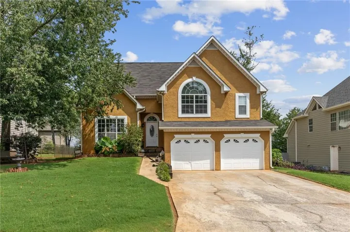 Stucco exterior with a two-car garage, arched window, and mature landscaping