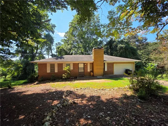 Ranch-style house featuring a chimney, brick siding, and an attached garage